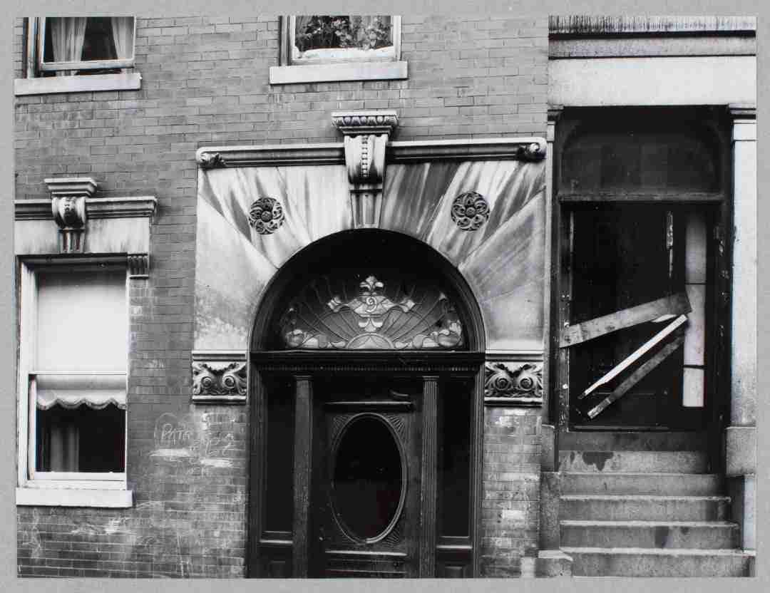 Black and white photograph of an arched doorway in a brick apartment building.
